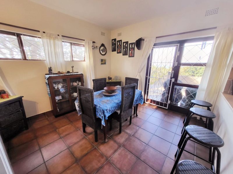 A dining area featuring terracotta floor tiles, large windows, and a security gate leading to the exterior.