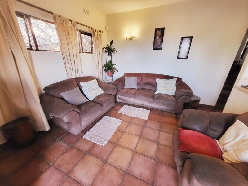 A cozy living room featuring terracotta floor tiles, wall-mounted lighting, and large windows with security bars, providing a functional and comfortable seating area.