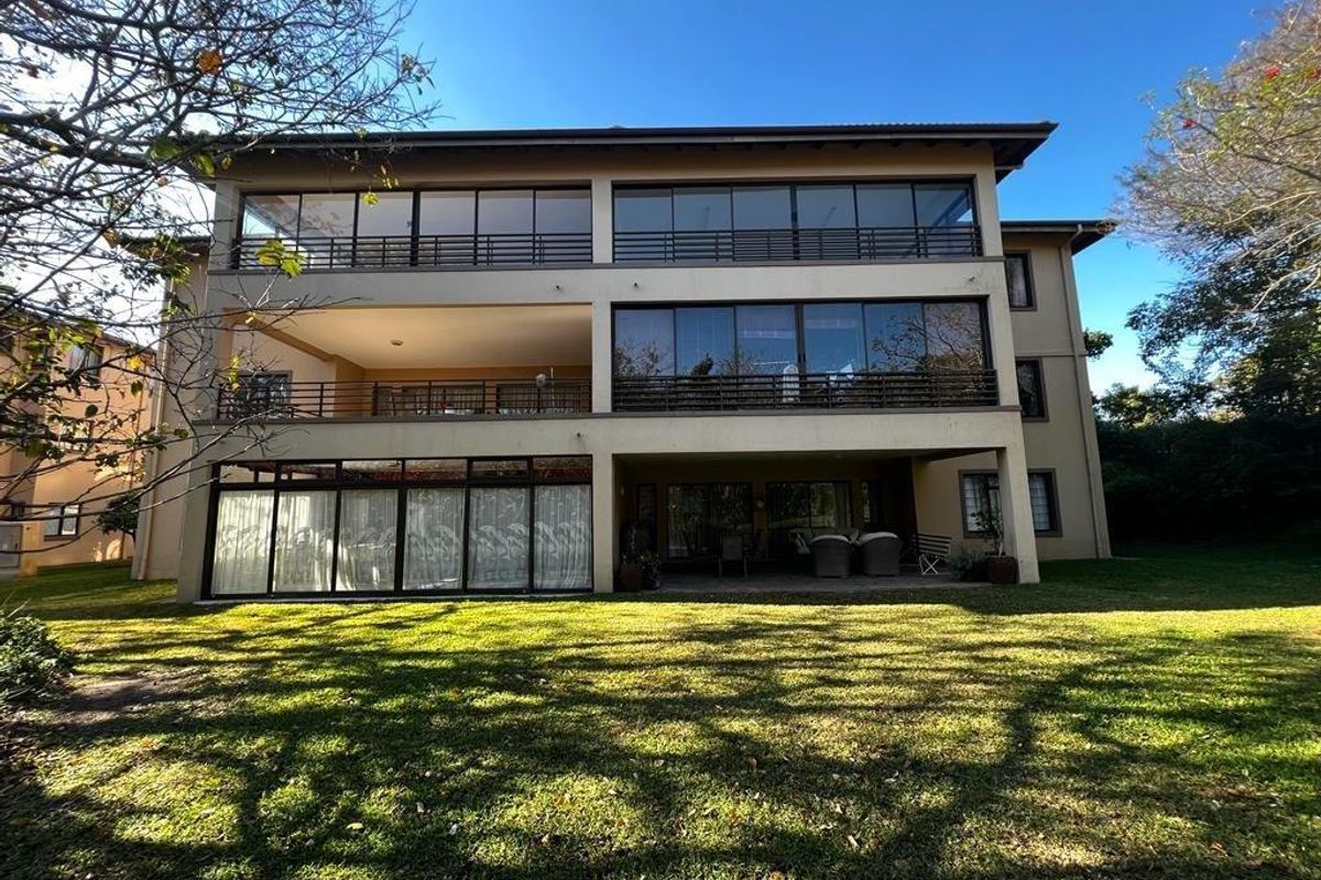 Rear view of a multi-story apartment building featuring expansive glass sliding doors, private balconies with railings, and a ground-floor covered patio area.
