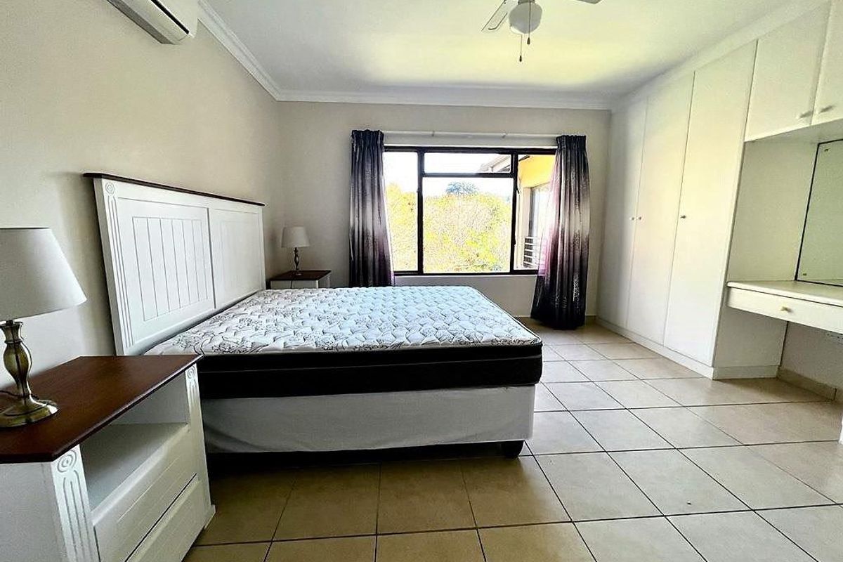 Spacious bedroom featuring tiled flooring, built-in cupboards with an integrated vanity, a ceiling fan, and a split-system air conditioner.