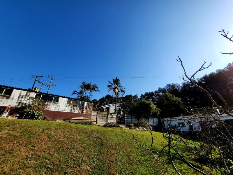 Rear view of the farm property showing sloped lawn, concrete boundary walls, and exterior building facades with visible signs of weathering and maintenance requirements.