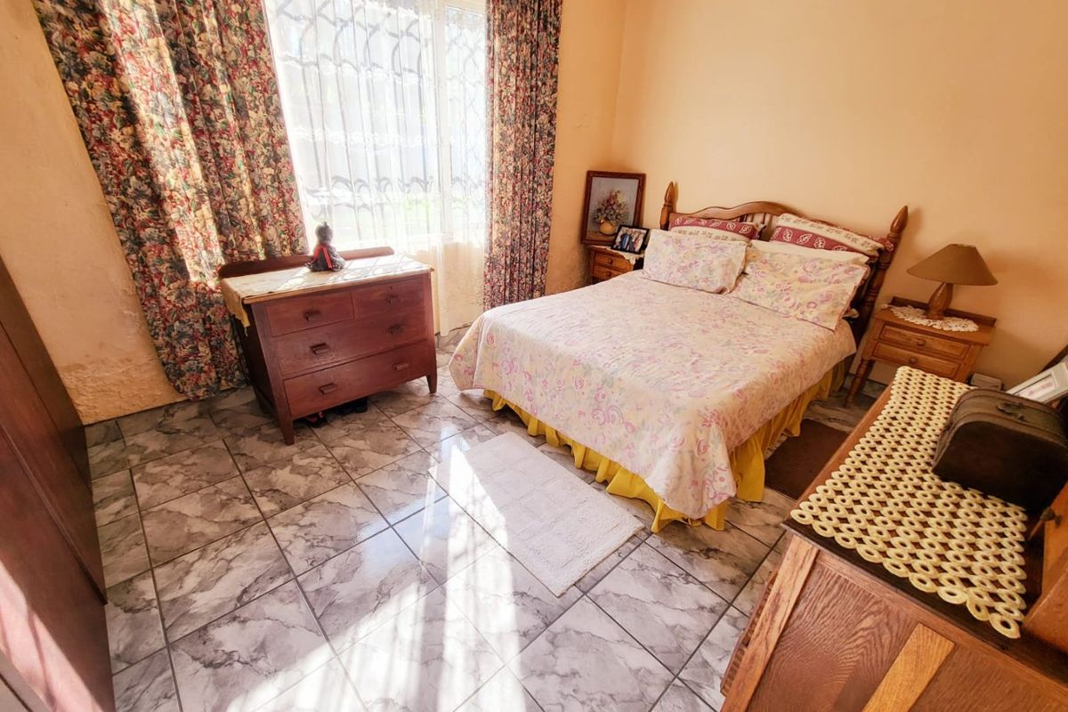A bedroom featuring tiled flooring and a large window with security bars, requiring cosmetic updates to the wall finishes.