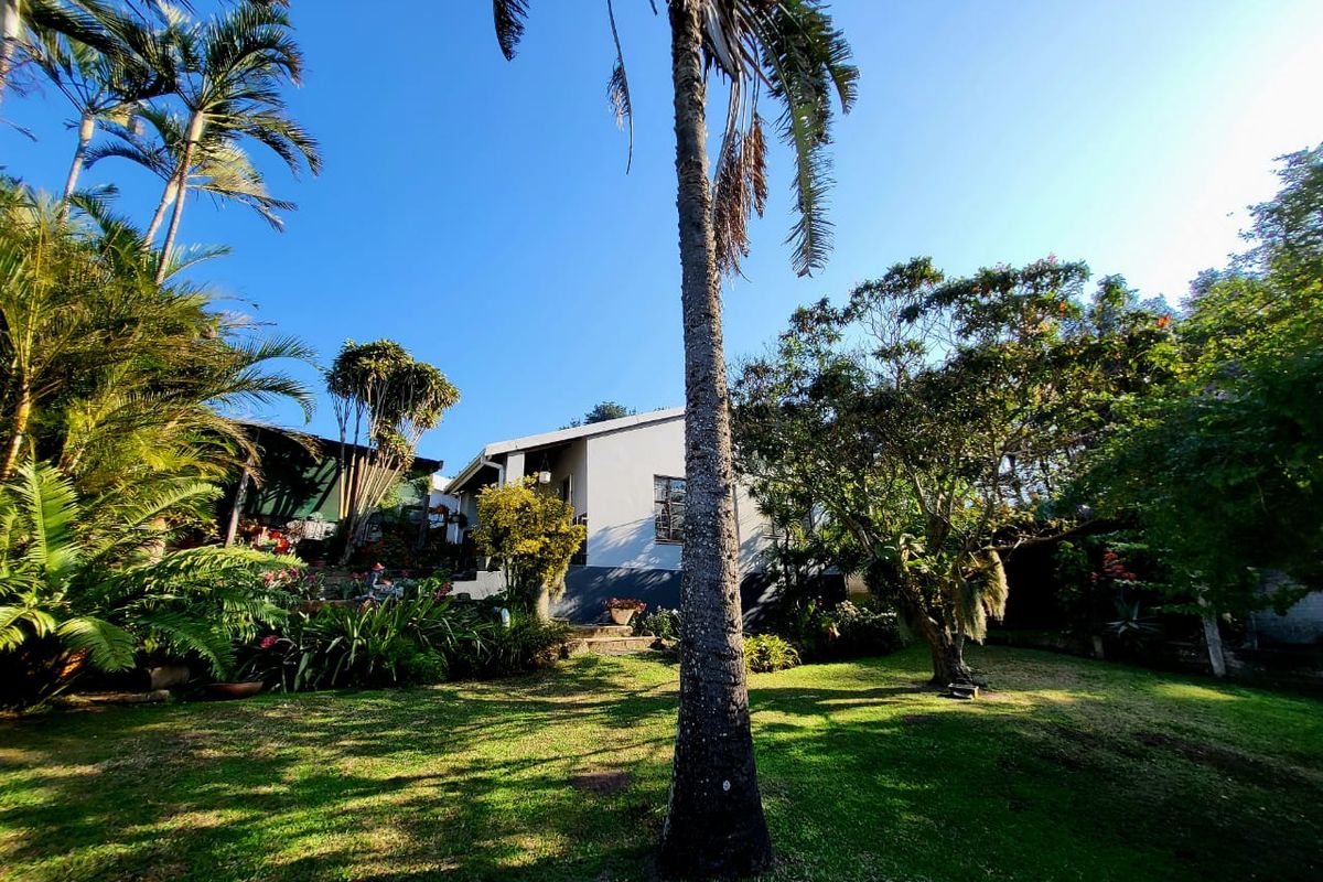 A view of the rear garden featuring mature trees, lush landscaping, and a well-maintained lawn leading towards the main dwelling.