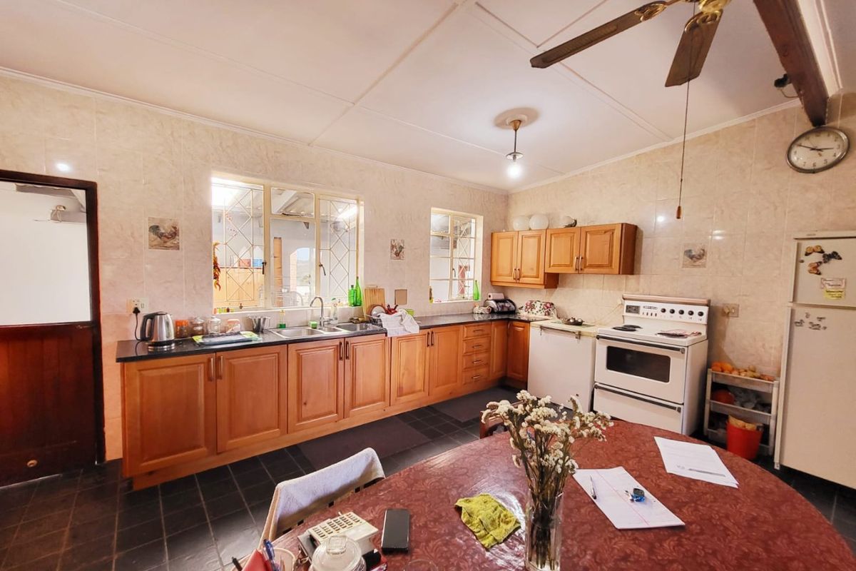 A functional kitchen featuring wooden cabinetry, tiled splashbacks, a double sink, and a freestanding oven, with tiled flooring throughout.