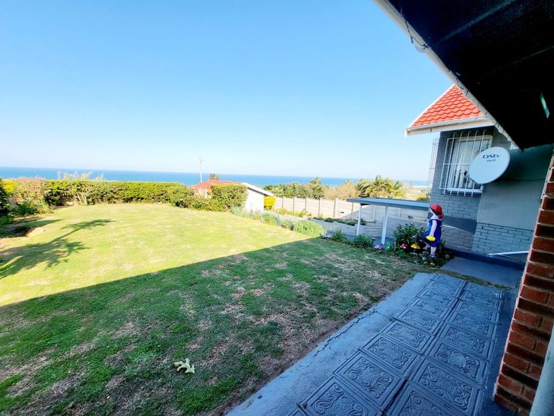 A rear garden view featuring a paved patio area, a lawn, and a distant ocean view from the property.