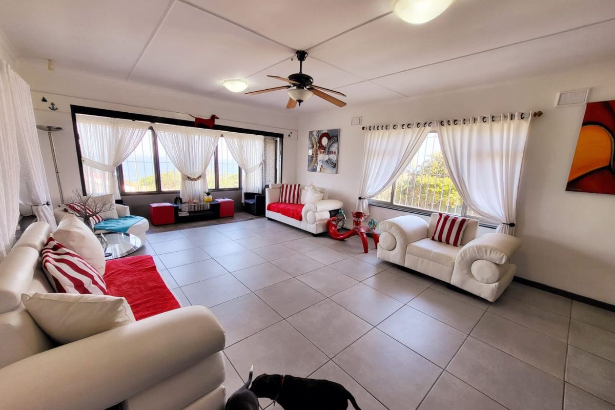 Spacious living room featuring large windows with security bars, tiled flooring, and a central ceiling fan, offering a bright and open layout.