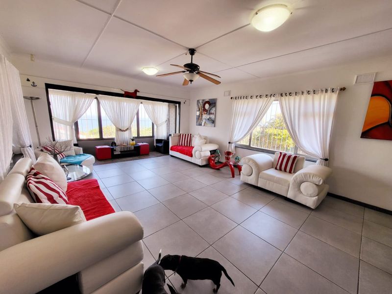 Spacious living room featuring large windows with security bars, tiled flooring, and a central ceiling fan, offering a bright and open layout.