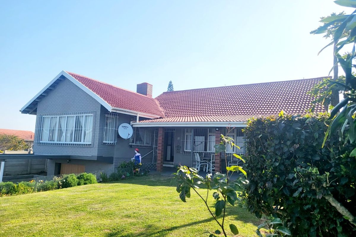 Rear view of a single-story house featuring a tiled roof, brick chimney, and a covered patio area overlooking a well-maintained garden.