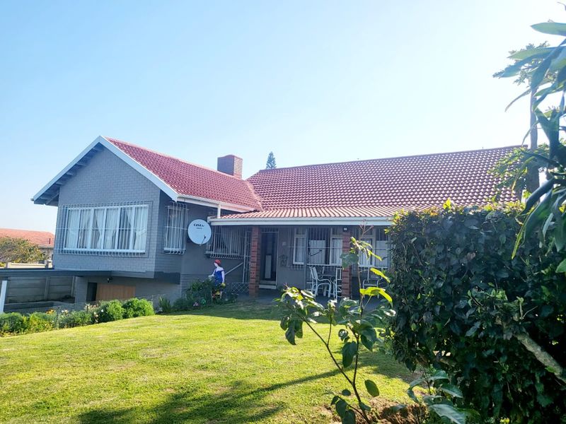 Rear view of a single-story house featuring a tiled roof, brick chimney, and a covered patio area overlooking a well-maintained garden.