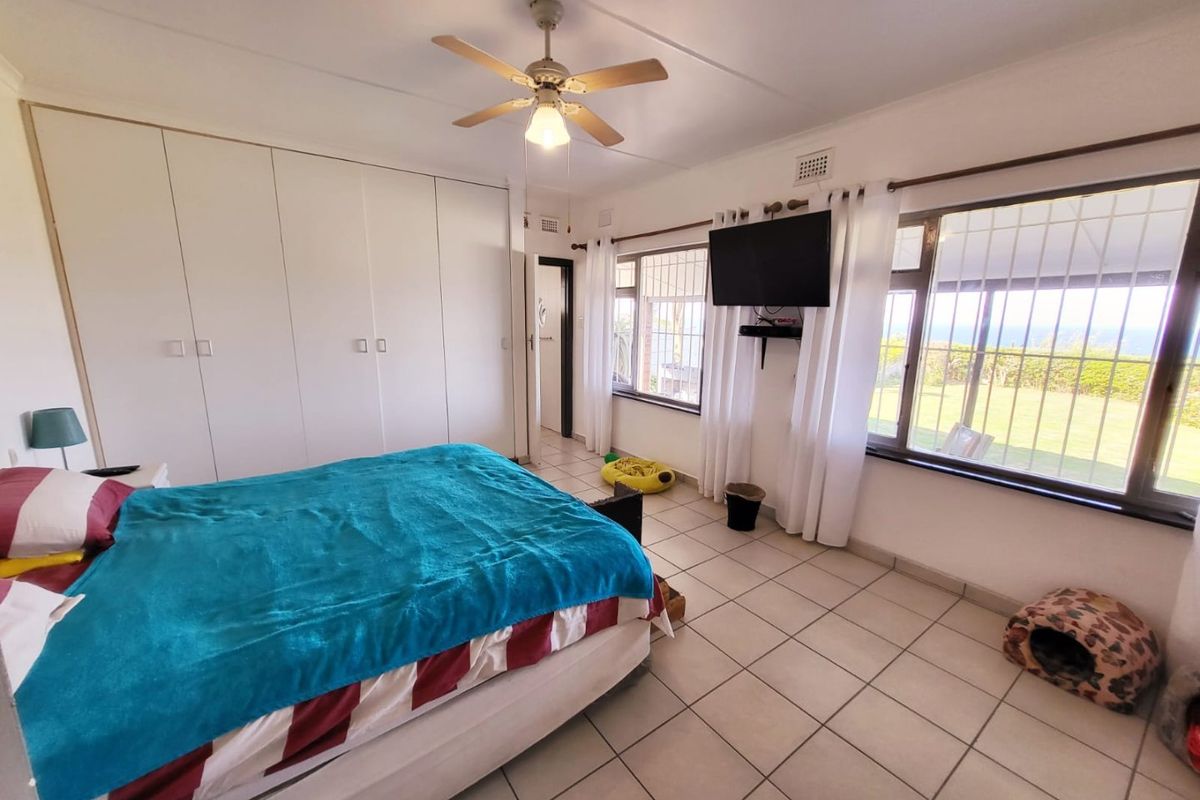 A spacious bedroom featuring built-in cupboards, tiled flooring, a ceiling fan, and large windows with security bars offering natural light.