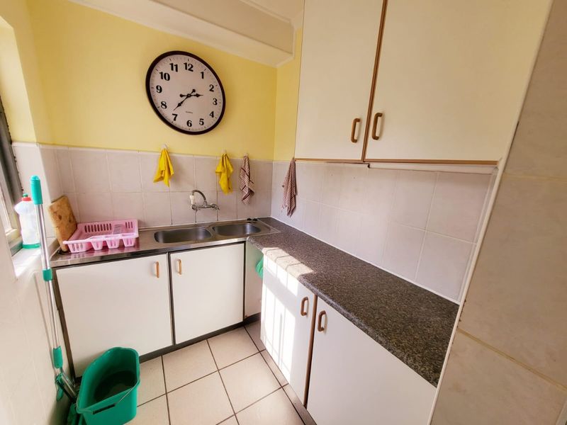 A functional scullery area featuring a double bowl stainless steel sink, laminate countertops, tiled splashback, and ample built-in cabinetry for storage.