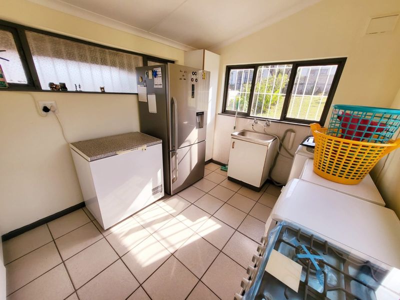 A functional laundry room featuring tiled flooring, a utility sink, and built-in cabinetry with natural light from the windows.