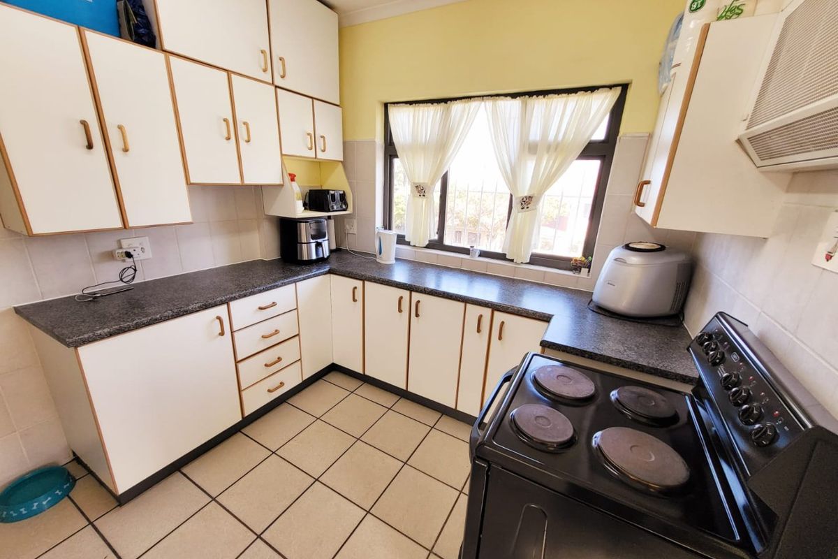 A functional kitchen featuring white cabinetry, dark laminate countertops, tiled flooring, and a tiled splashback, offering a clean and practical workspace.