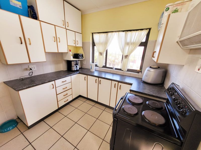 A functional kitchen featuring white cabinetry, dark laminate countertops, tiled flooring, and a tiled splashback, offering a clean and practical workspace.