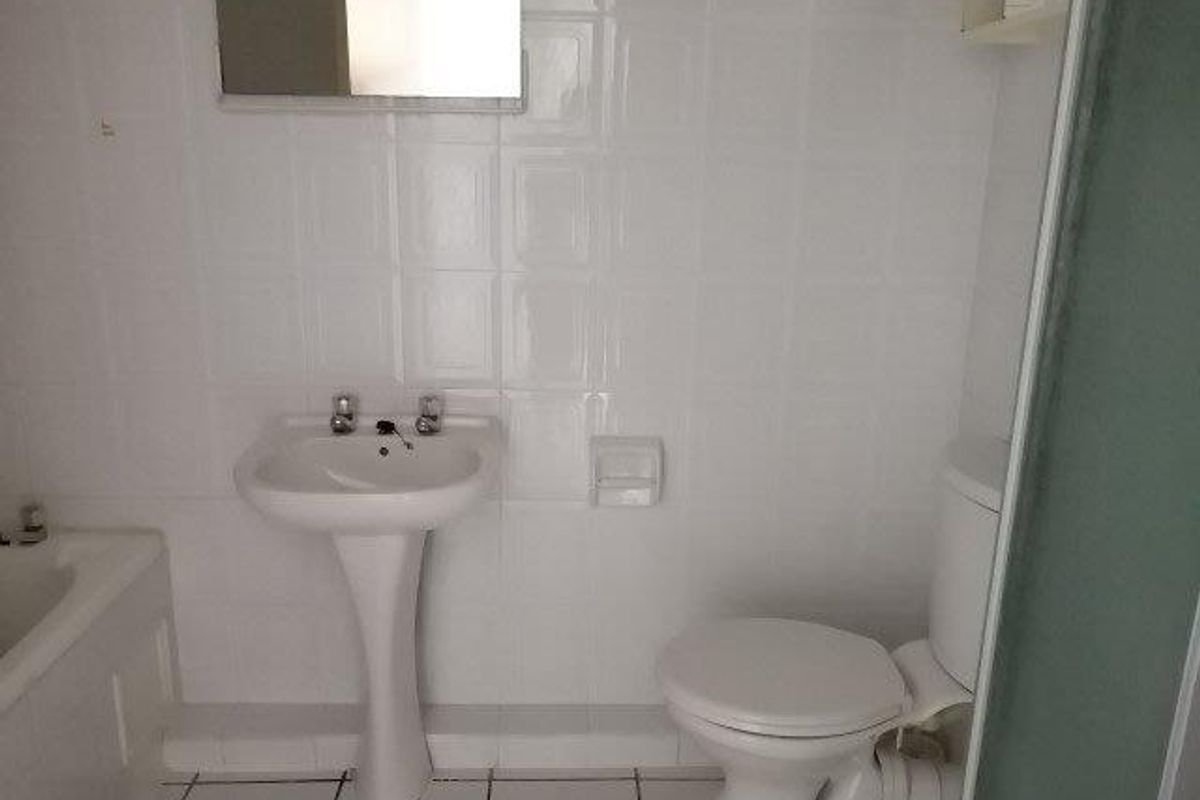 A dated bathroom featuring a pedestal basin, toilet, and bathtub with white ceramic wall and floor tiles.