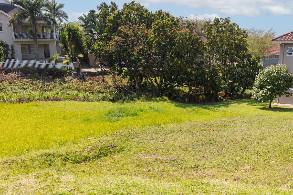A view of a vacant residential plot featuring established trees and surrounding residential properties.