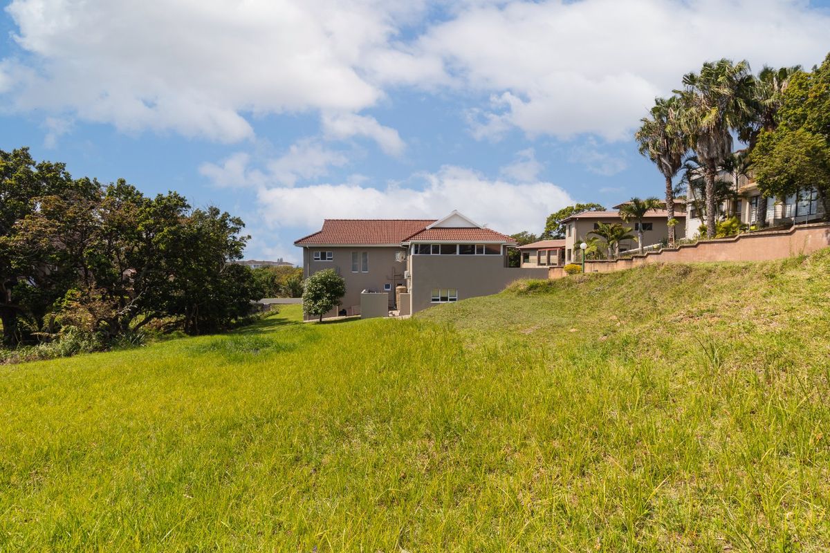 A view of the vacant residential land featuring a gentle slope, established grass, and mature trees, with neighboring residential properties visible in the background.