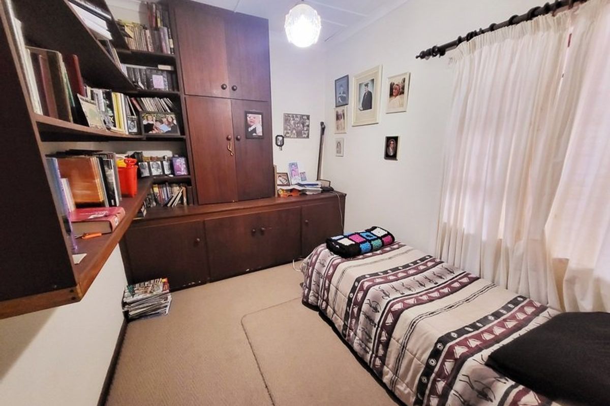 A bedroom featuring built-in wooden cabinetry and shelving, providing ample storage space, with neutral carpeting and window treatments.