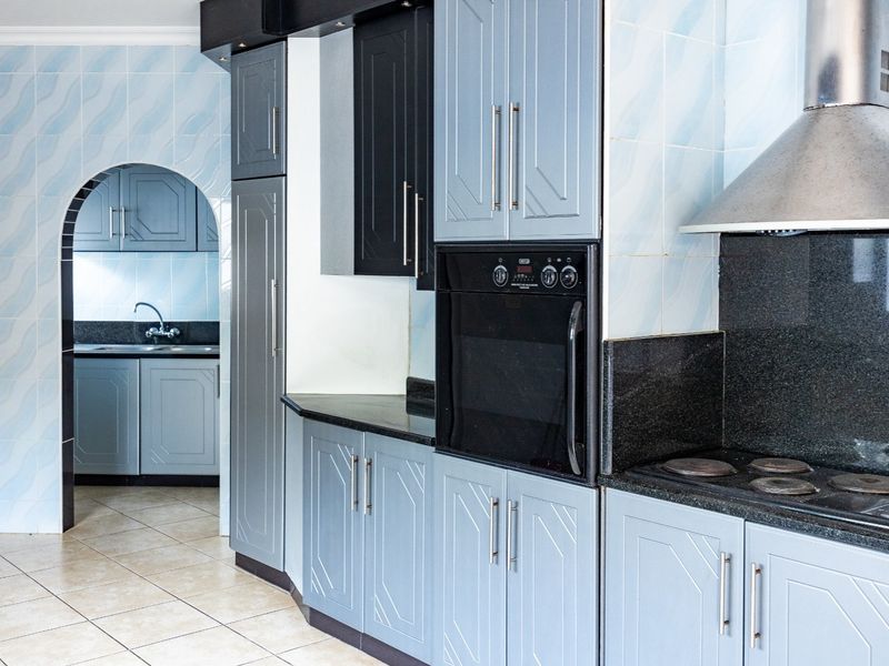 A functional kitchen featuring grey cabinetry, granite countertops, built-in oven, and hob, with an adjoining scullery area accessible through a classic archway.