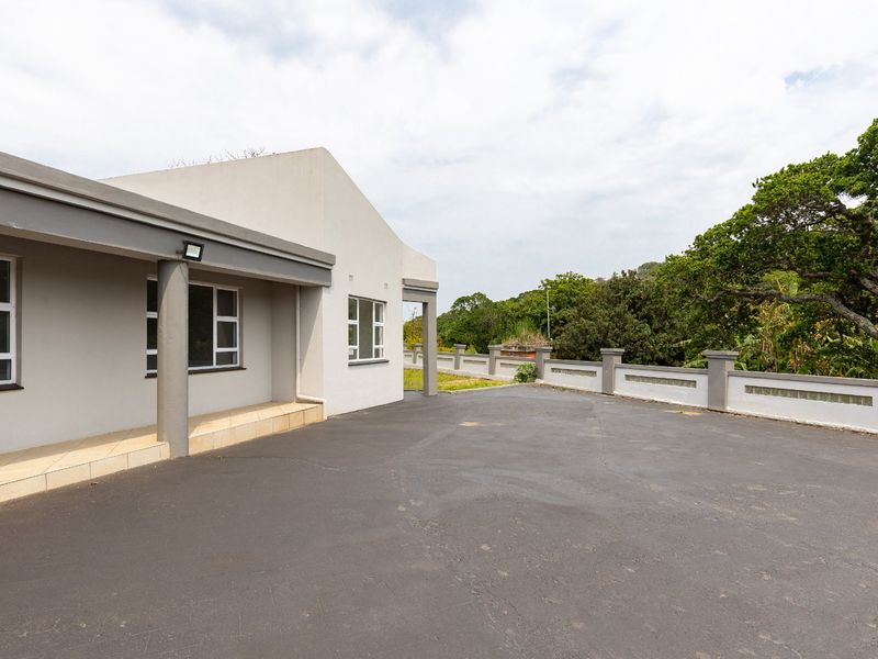 A spacious asphalt driveway leading to a covered patio area with concrete columns, featuring a perimeter wall with decorative glass block inserts.