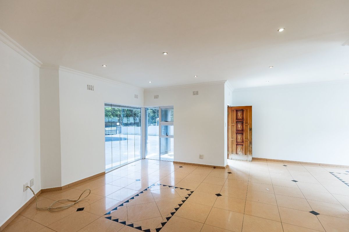 Spacious, empty living area featuring neutral tiled flooring, recessed downlighting, and direct access to the exterior through a sliding glass door.