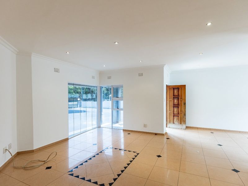 Spacious, empty living area featuring neutral tiled flooring, recessed downlighting, and direct access to the exterior through a sliding glass door.