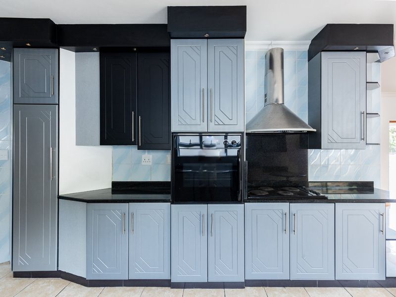 A functional kitchen featuring two-tone cabinetry, granite countertops, a built-in oven, and a stainless steel extractor fan with tiled finishes.
