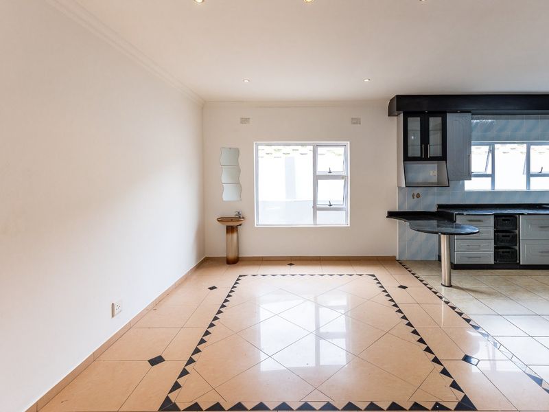 Open plan living and kitchen area featuring tiled flooring, built-in cabinetry with granite countertops, and a small pedestal basin.