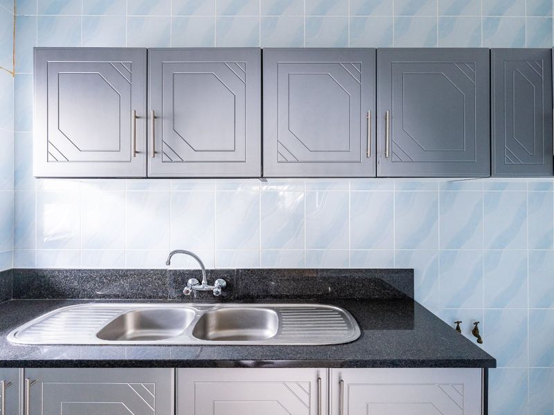 A clean kitchen area featuring a double bowl stainless steel sink, dark granite countertops, and light grey cabinetry with a decorative tiled backsplash.