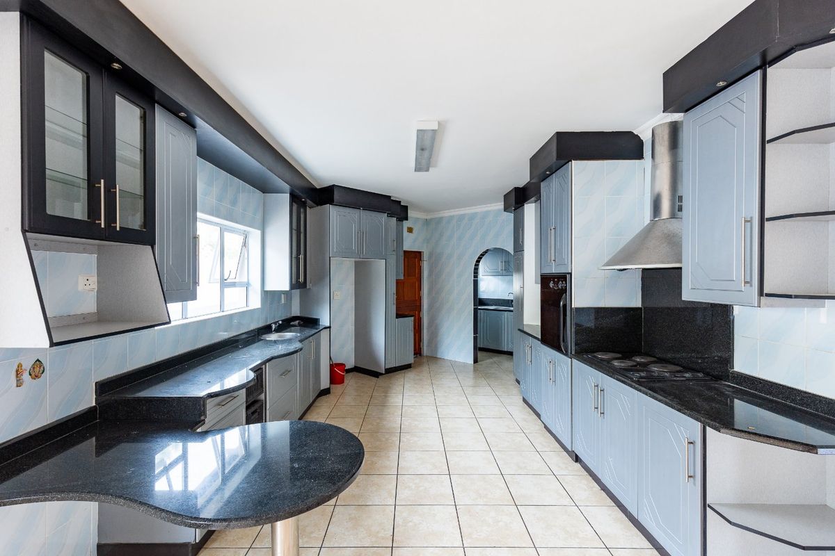 Spacious kitchen featuring granite countertops, built-in cabinetry, integrated oven and hob, and tiled flooring, offering a functional layout with an adjacent scullery area.