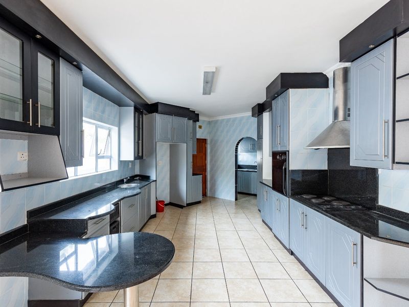 Spacious kitchen featuring granite countertops, built-in cabinetry, integrated oven and hob, and tiled flooring, offering a functional layout with an adjacent scullery area.