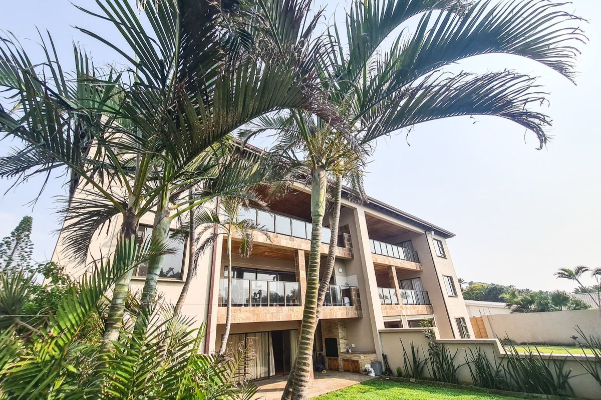 Rear view of the apartment building featuring multiple balconies with glass balustrades, stone cladding accents, and a ground-floor patio with a built-in braai.