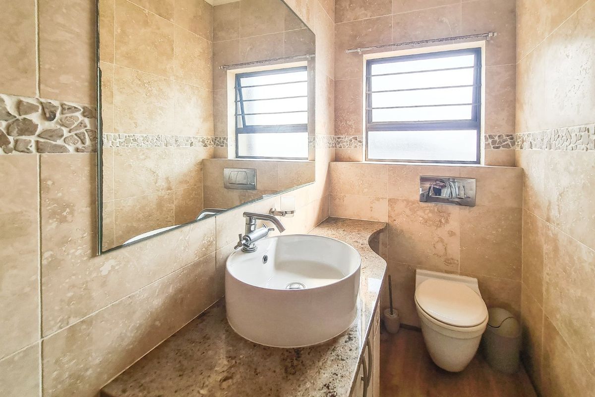 A modern bathroom featuring a vessel sink on a granite vanity, wall-mounted toilet with concealed cistern, and neutral stone-look wall tiling.