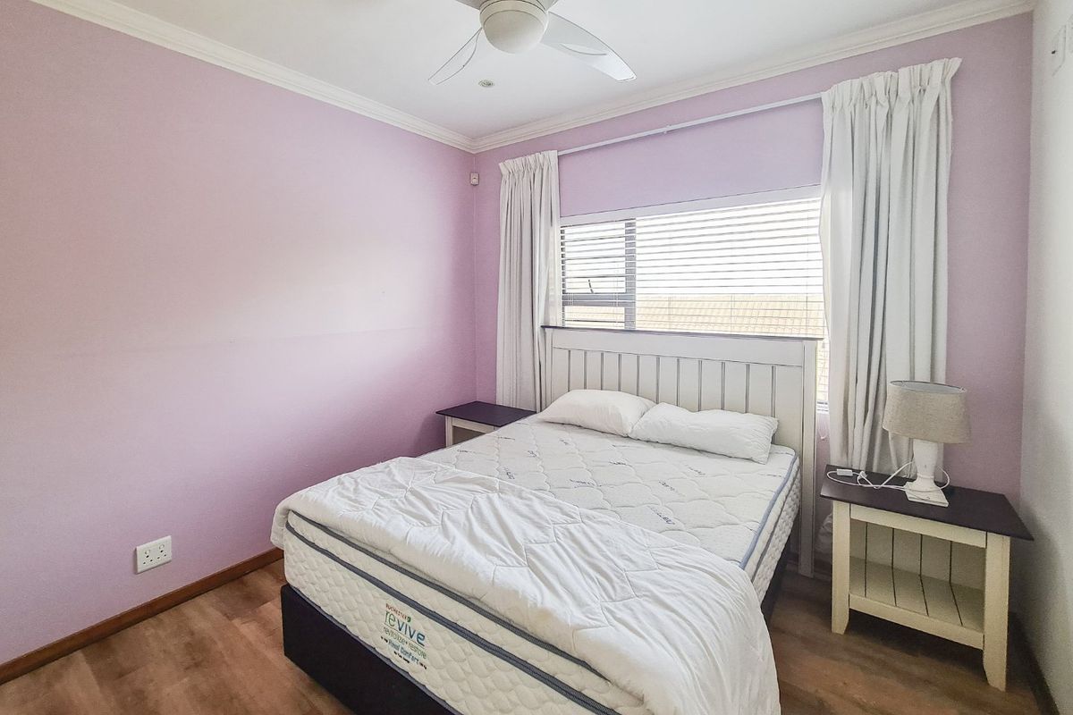 A bedroom featuring laminate flooring, a ceiling fan, and large windows with venetian blinds, providing a functional and well-lit sleeping space.