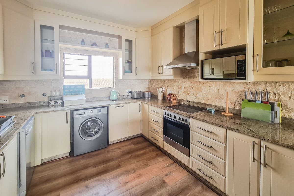 A well-appointed kitchen featuring cream cabinetry, granite countertops, stone backsplash, and integrated appliances including an oven, hob, and extractor fan.
