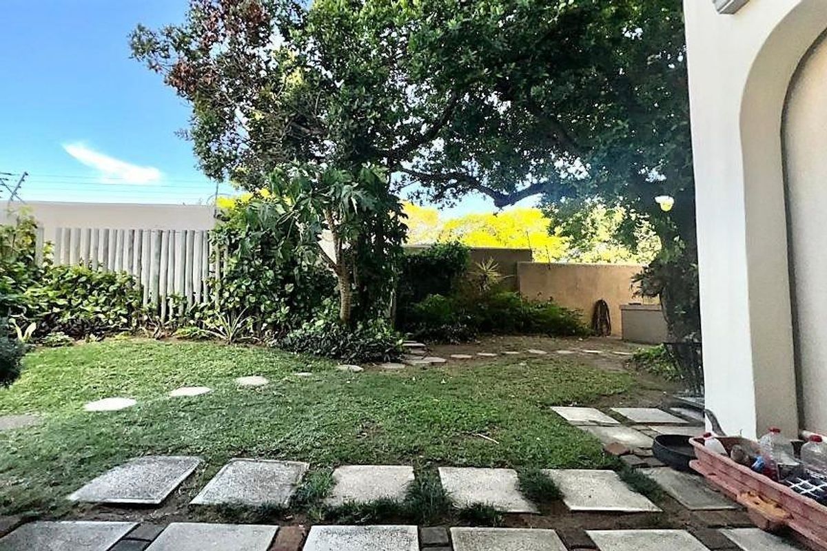 A private rear garden area featuring a paved walkway, established trees, and perimeter boundary walls.