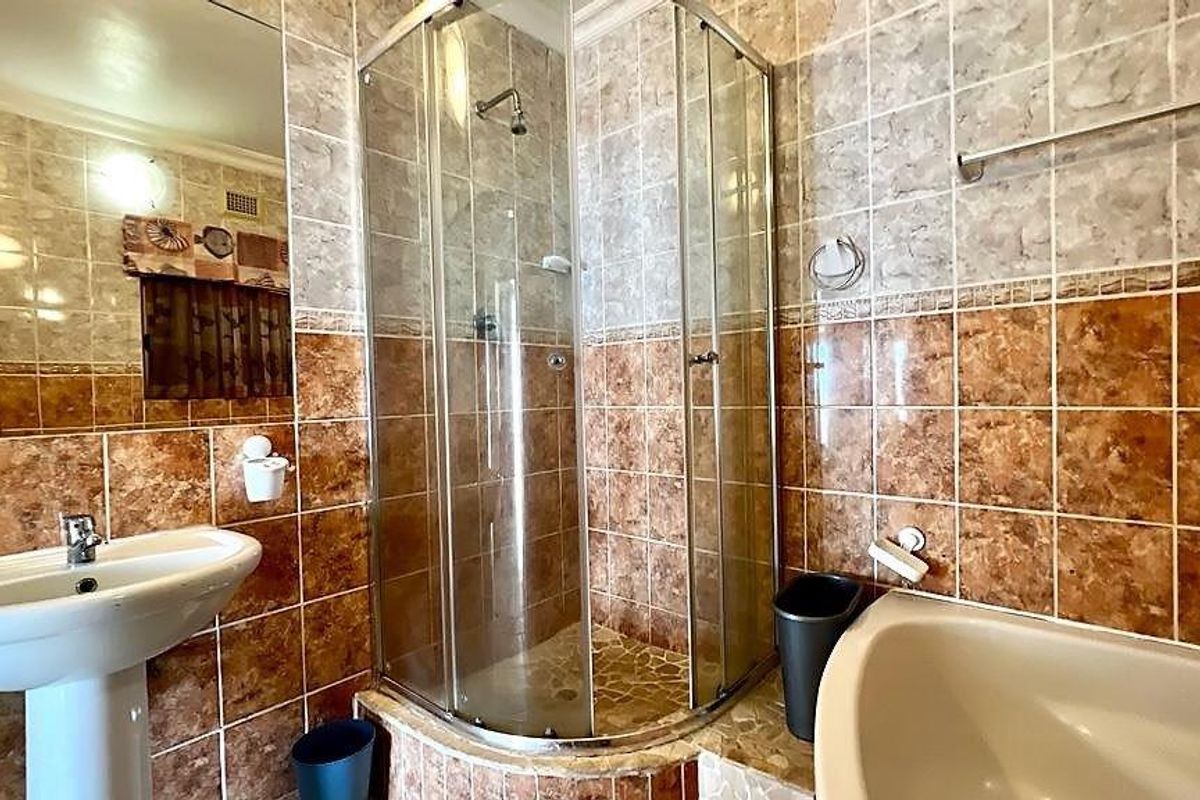 A functional bathroom featuring a corner shower enclosure, a separate bathtub, and a pedestal sink with full-height wall tiling.