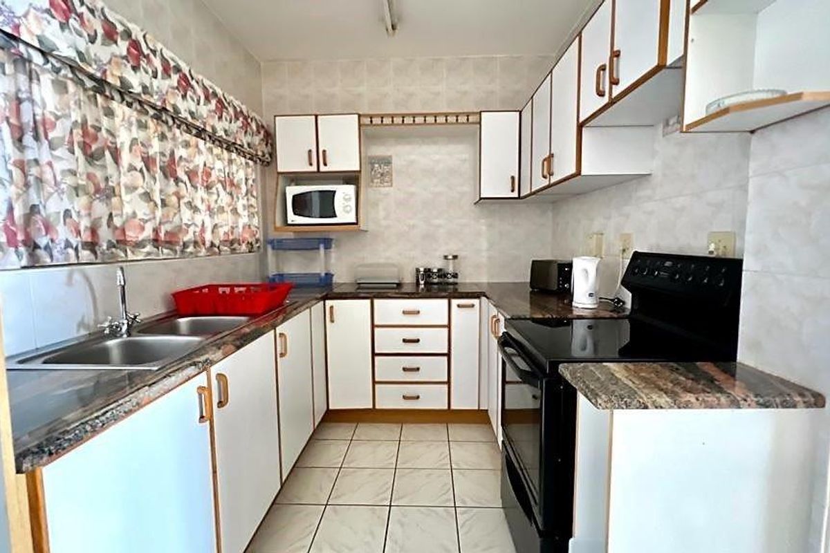 A functional kitchen featuring white cabinetry, laminate countertops, a double basin sink, and a freestanding stove with tiled flooring and splashbacks.