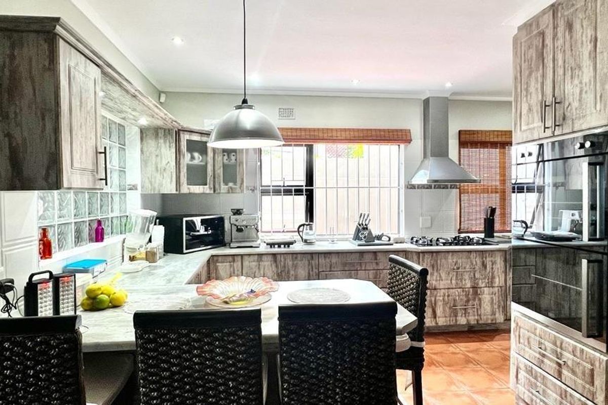 A functional kitchen featuring wood-look cabinetry, stone-effect countertops, a gas hob, built-in oven, and a unique glass block feature wall.