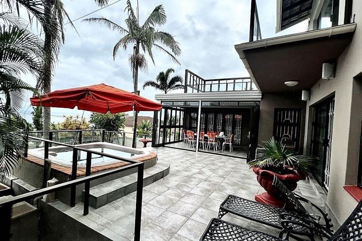 Rear patio area featuring a tiled terrace, built-in spa, glass balustrades, and direct access to the interior living space through sliding doors.