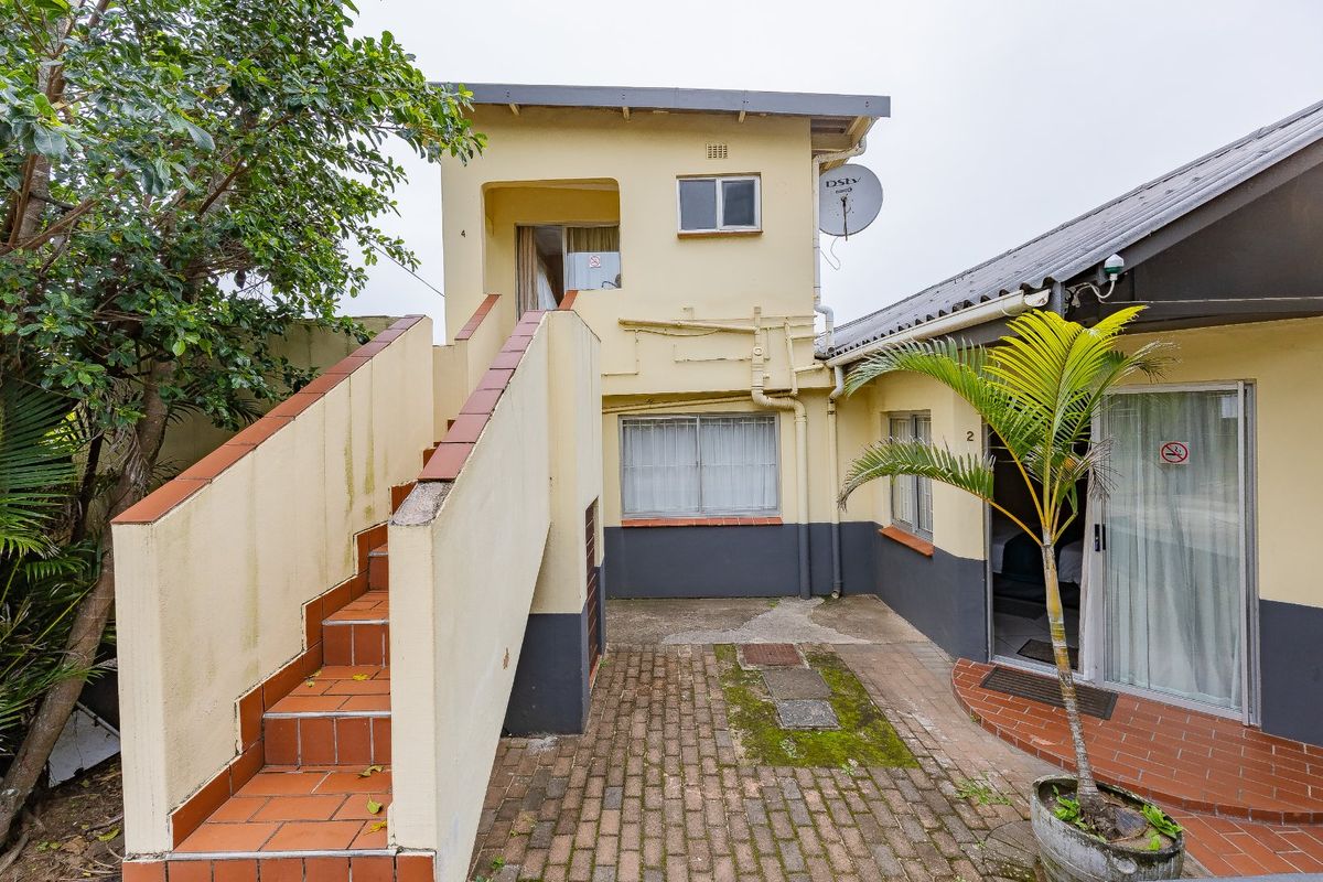 Rear exterior view of a two-story residential building featuring an external staircase, brick paved courtyard, and sliding door access to the ground floor unit.