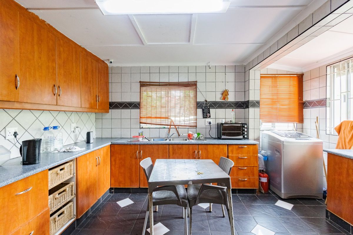 A functional kitchen featuring wood-look laminate cabinetry, tiled backsplash, and dark tiled flooring, offering a practical layout with integrated sink and ample storage space.