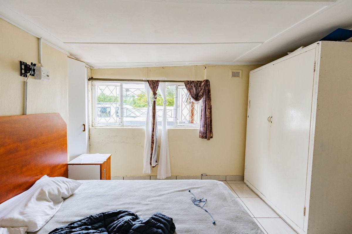 A bedroom featuring tiled flooring, a built-in wardrobe, and security bars on the windows. The room requires cosmetic updates to improve its overall condition.