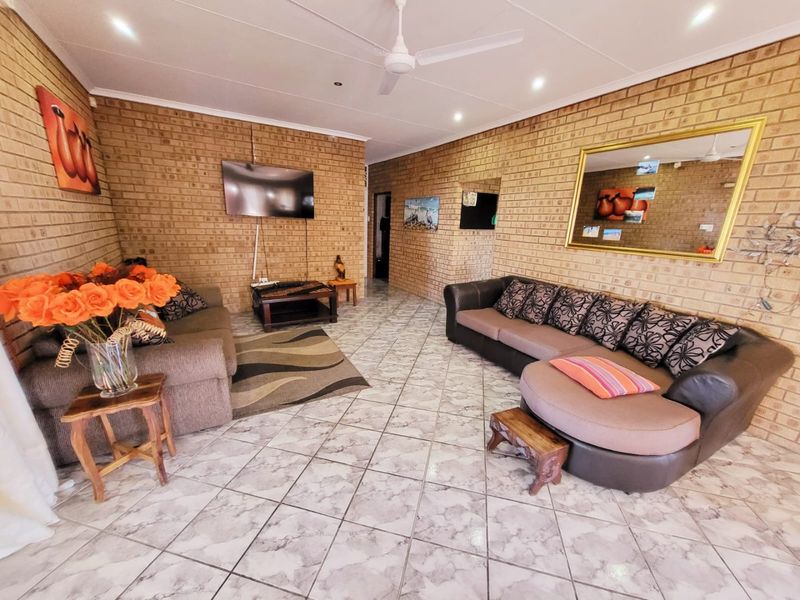 Spacious living room featuring exposed brick walls, tiled flooring, and a ceiling fan, offering a rustic and comfortable atmosphere.