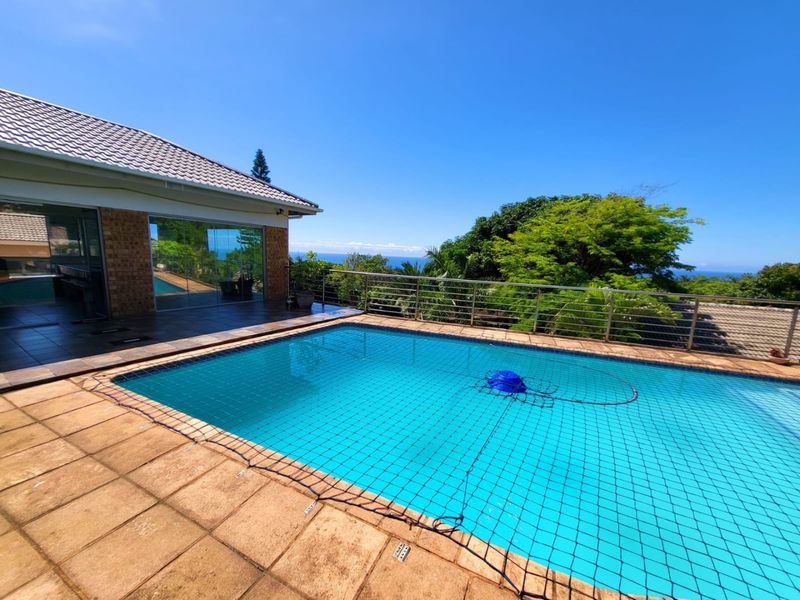 Outdoor pool area featuring a tiled deck, safety net, and stainless steel balustrade with scenic views and direct access to the home.