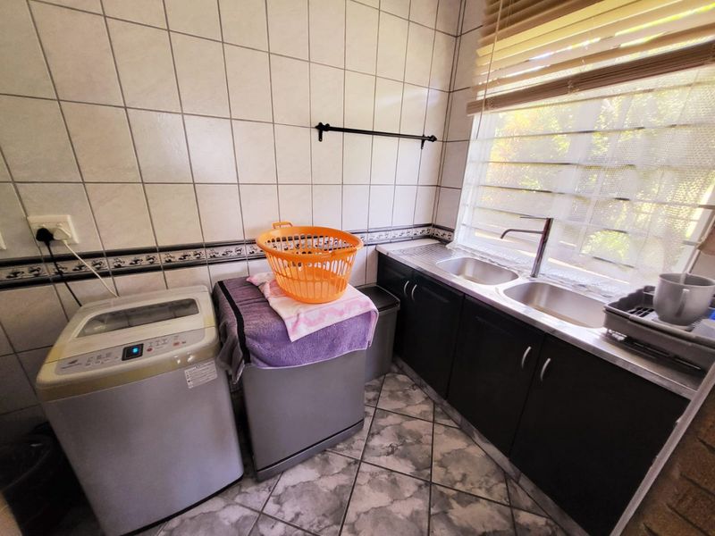 A functional laundry room featuring tiled walls and flooring, built-in cabinetry with a double sink, and natural light through venetian blinds.