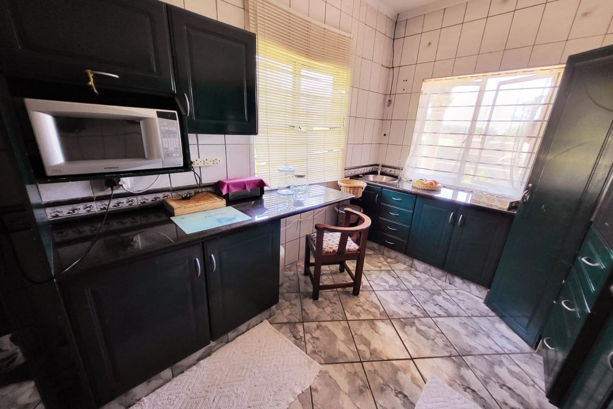 A functional kitchen featuring dark cabinetry, granite countertops, built-in microwave, and tiled finishes throughout, offering a practical layout with natural light.