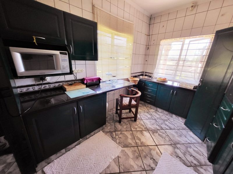 A functional kitchen featuring dark cabinetry, granite countertops, built-in microwave, and tiled finishes throughout, offering a practical layout with natural light.