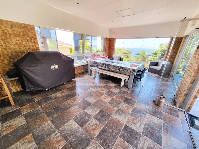 Spacious covered patio featuring tiled flooring, exposed brick walls, and large sliding glass doors offering scenic views.