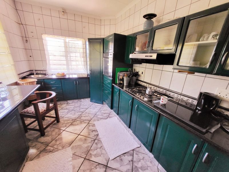 A functional kitchen featuring dark green cabinetry, granite countertops, a gas hob, and an integrated oven with tiled finishes throughout.